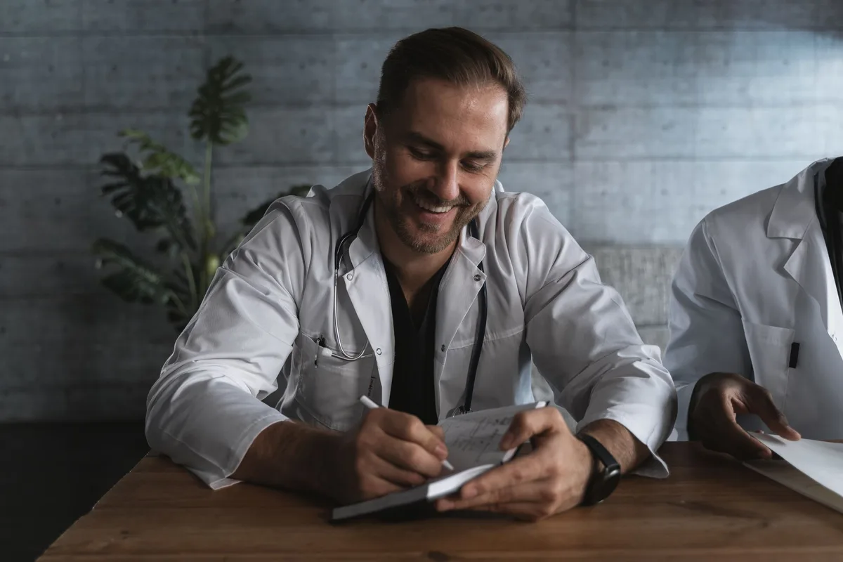 A physician taking notes while listening to a patient during an intake consultation.