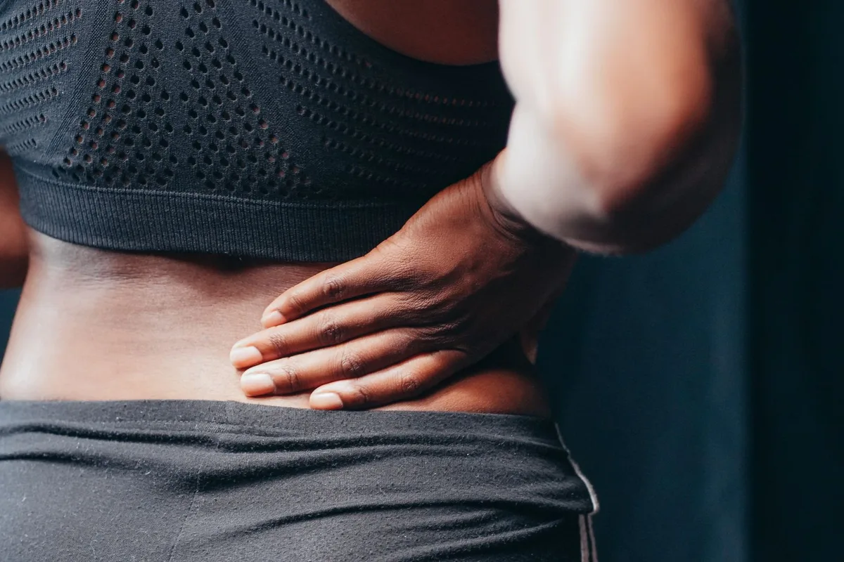 An older adult holding their lower back while standing in a doorway.