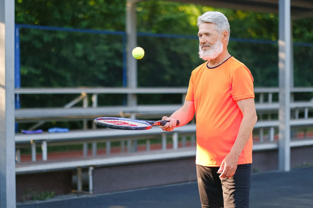 An active older adult pausing on a tennis court, holding a knee.