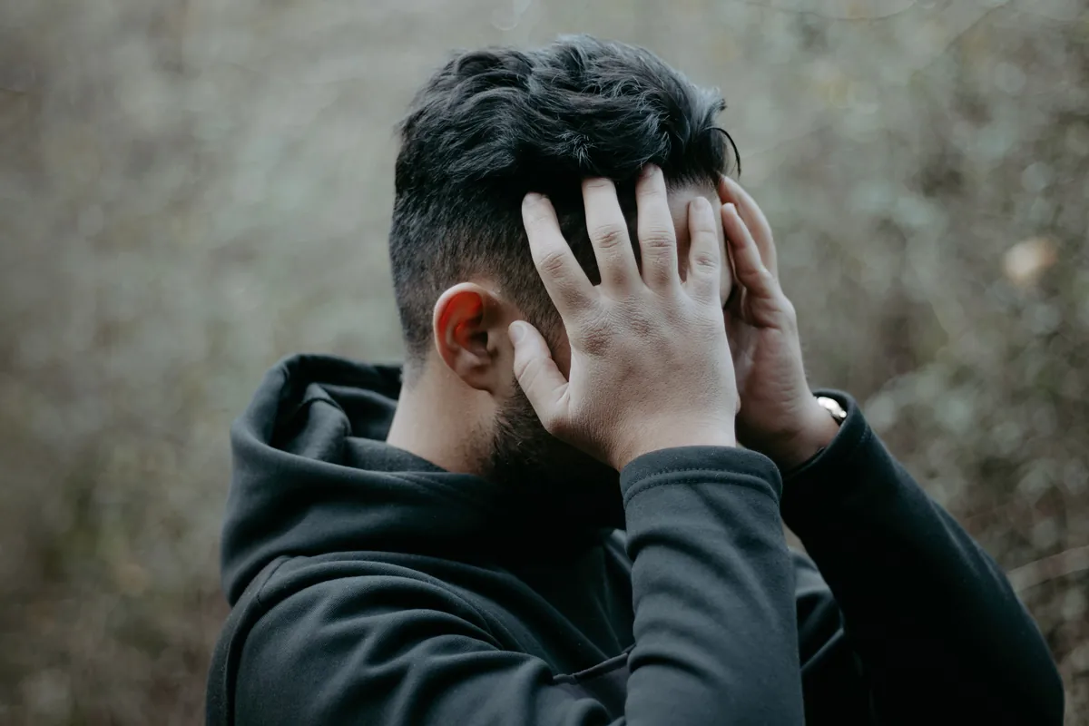 A man pressing both hands against the back of his head in pain.