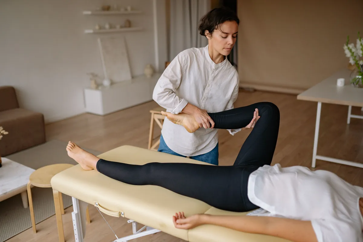 A clinician raising a patient's straightened leg while she lies on an exam table.