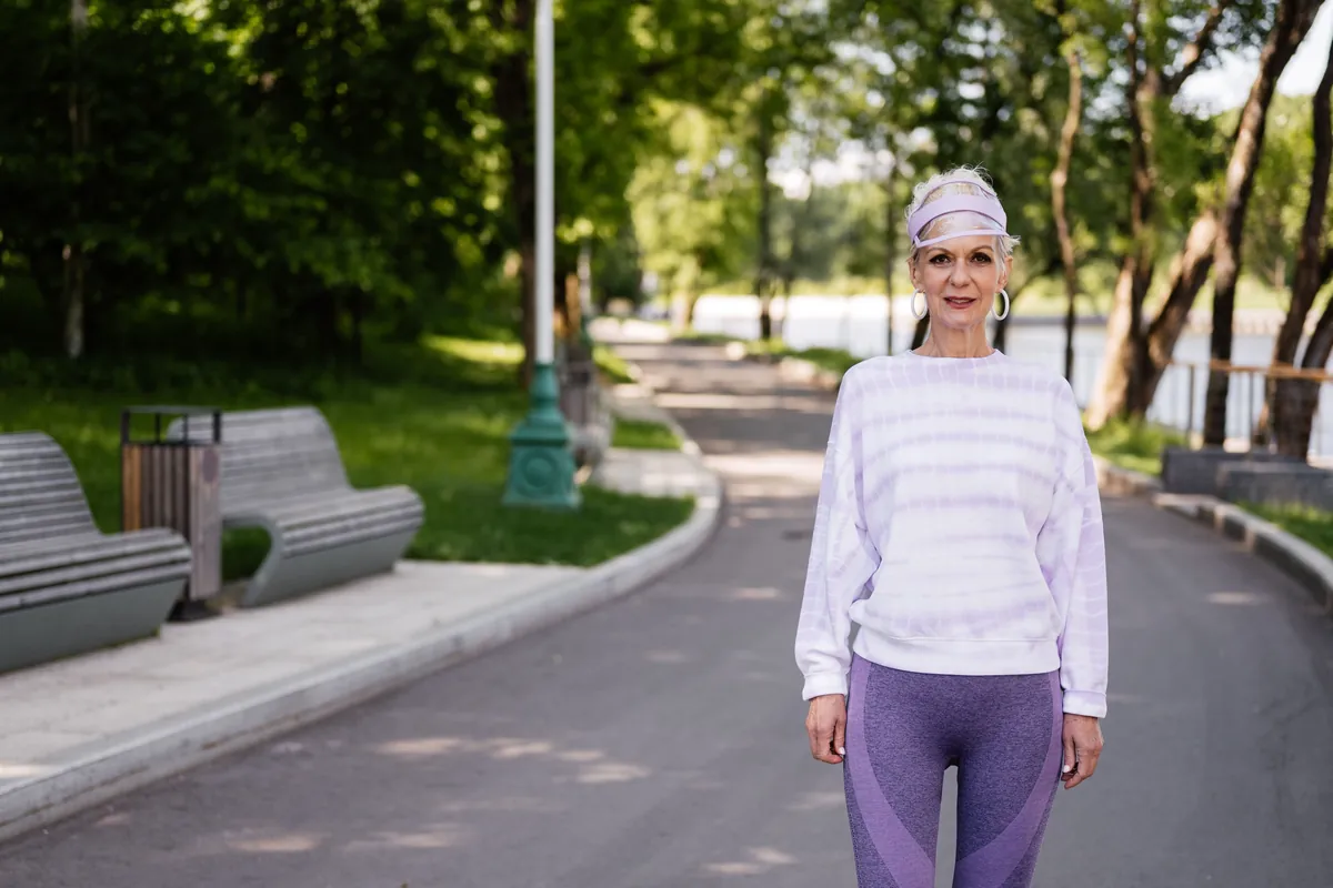 An older woman in activewear taking a walk outdoors in bright daylight.