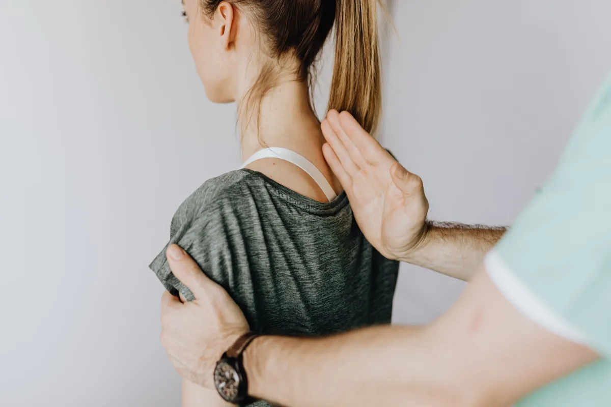 A clinician tracing a patient's spine with his fingers during a back exam.