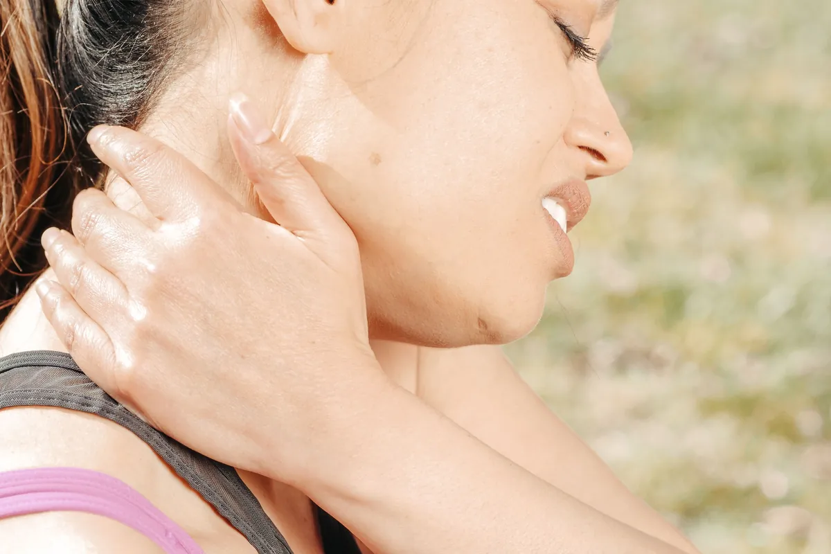 A woman wincing and holding the side of her sore neck.
